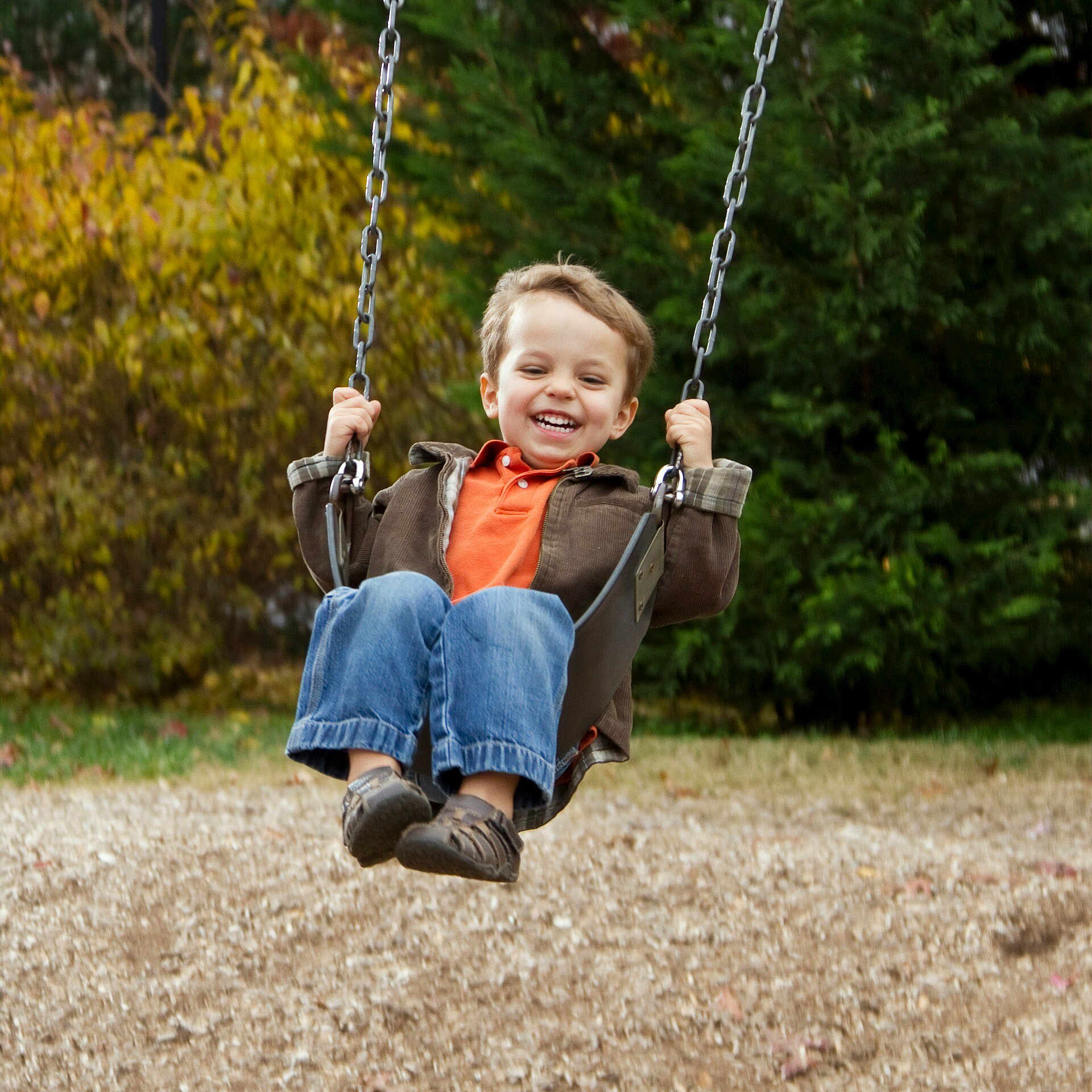 Junge lachend auf Schaukel auf einem Spielplatz