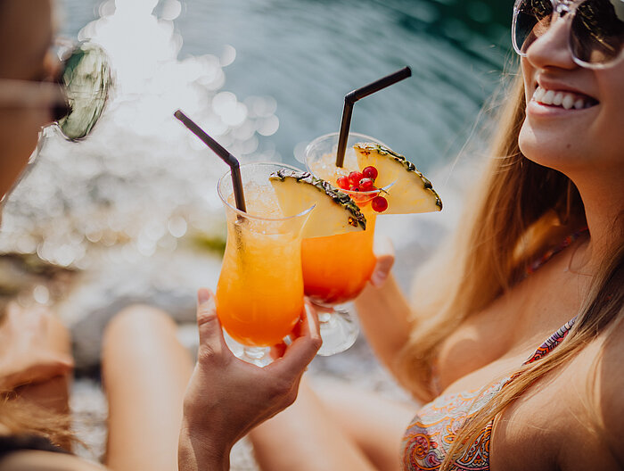 Zwei Frauen stoßen mit Cocktails am Bergseepool im Lürzerhof an