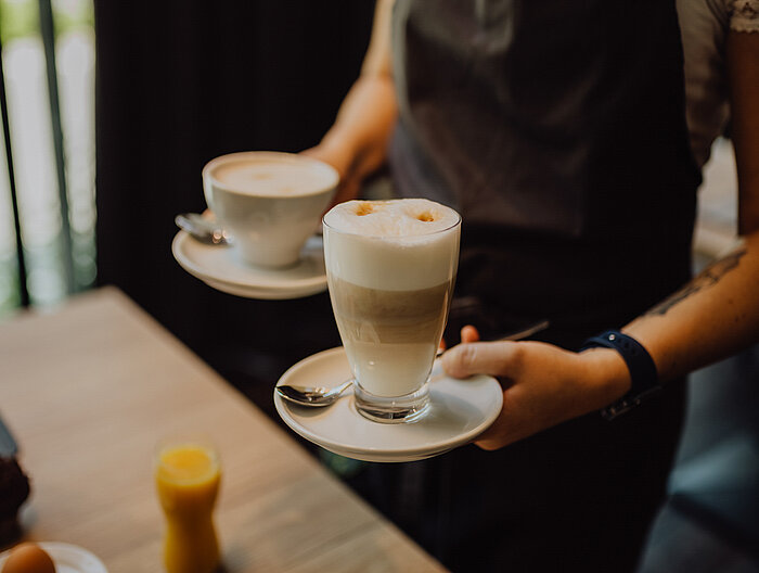 Eine Servicekraft mit zwei Tassen Kaffee in den Händen im Gourmet & Wellnesshotel Lürzerhof