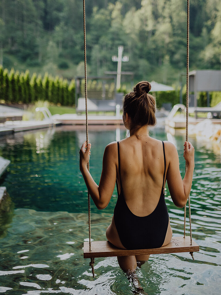 Adults Only SPA Eine Frau schwingt auf einer Schaukel über dem Naturpool im Wellnesshotel Lürzerhof in Salzburg.