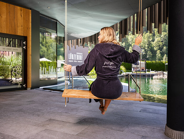 Schaukel_Saunabereich_Frau Frau im Bademantel auf einer Schaukel im Spa-Bereich mit Naturblick.