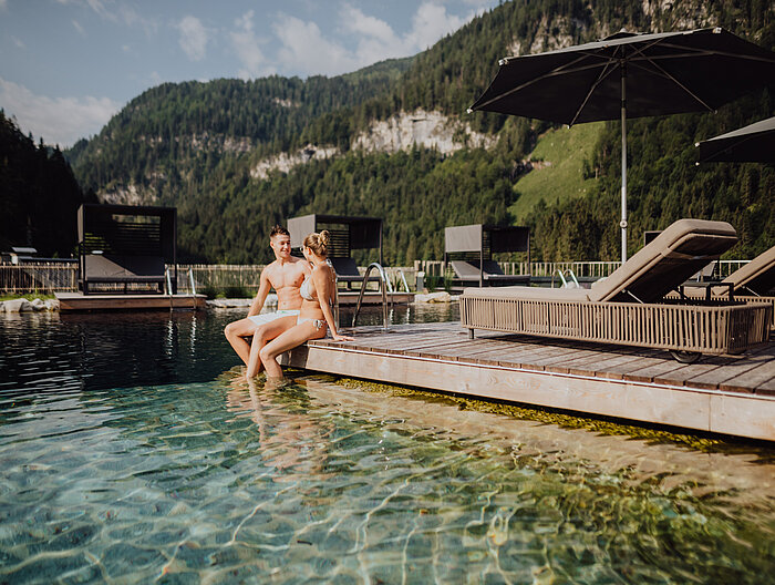 Ein Paar sitzt entspannt am Steg des Naturpools im Wellnesshotel Lürzerhof in Salzburg.