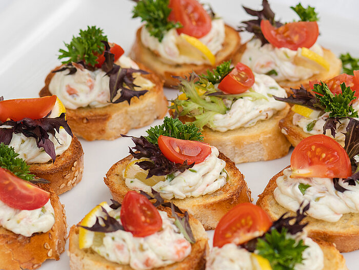 Closeup of delicious canape served on white plate Canapés mit Creme, Tomate, Zitrone und Kräutern auf Weißbrot