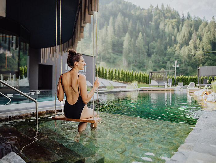 Eine Frau schaukelt über den Naturpool im Adults Only Bereich des Wellnesshotels Lürzerhof in Salzburg