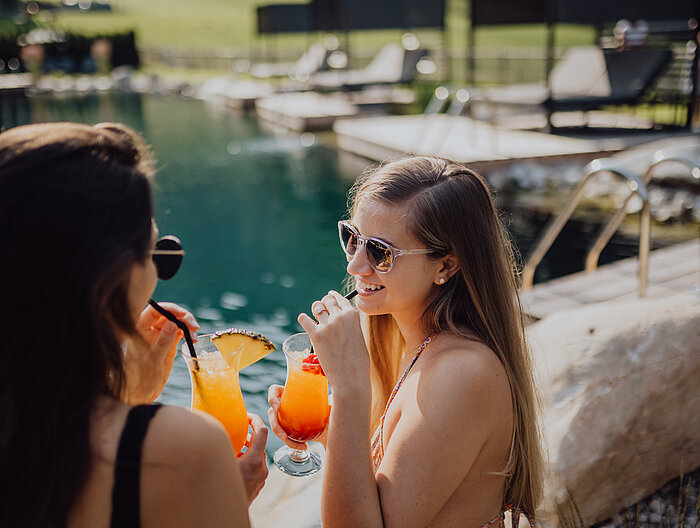 Zwei Frauen stoßen mit Cocktails am Bergseepool im Lürzerhof an