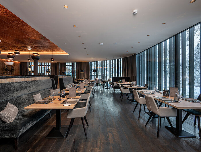 Ein stilvoll gedeckter Restaurantbereich im Lürzerhof Gourmet & Wellnesshotel mit Panoramablick auf die verschneite Berglandschaft.