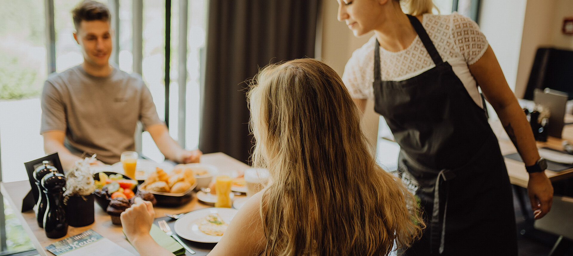 Ein Paar genießt das Frühstück im Lürzerhof Gourmet & Wellnesshotel, während sie von einer freundlichen Servicekraft bedient werden.