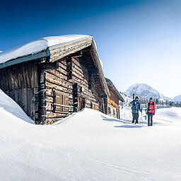 TVB_Shoot2 Zwei Skitourengeher vor verschneiter Berghütte bei strahlendem Winterwetter in Obertauern