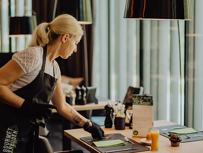 Eine Servicekraft bereitet mit Sorgfalt einen Frühstückstisch im Lürzerhof Gourmet & Wellnesshotel vor.