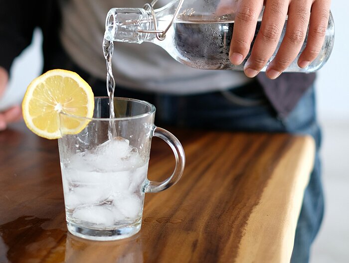 Mann gießt Wasser aus Glasflasche in Eisteeglas mit Zitrone