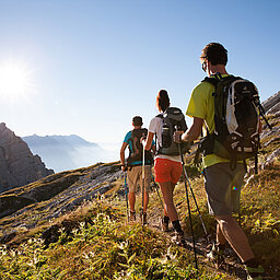 Wandern Wandergruppe mit Trekkingstöcken auf Bergpfad bei Sonnenschein